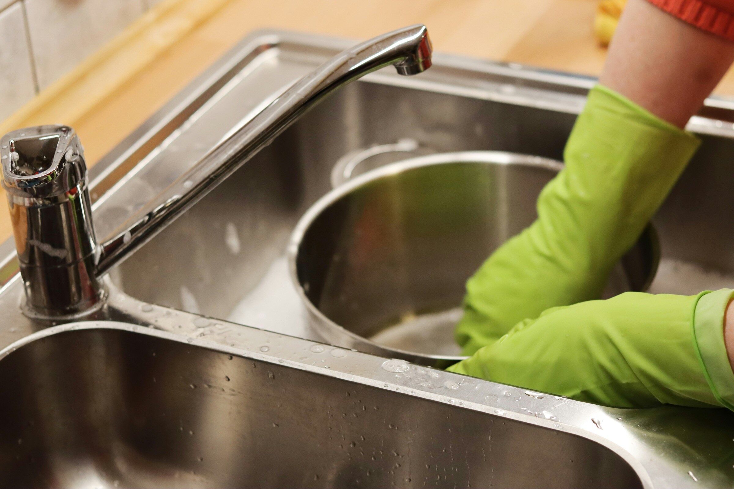 Gloved hands cleaning a pot in a steel sink