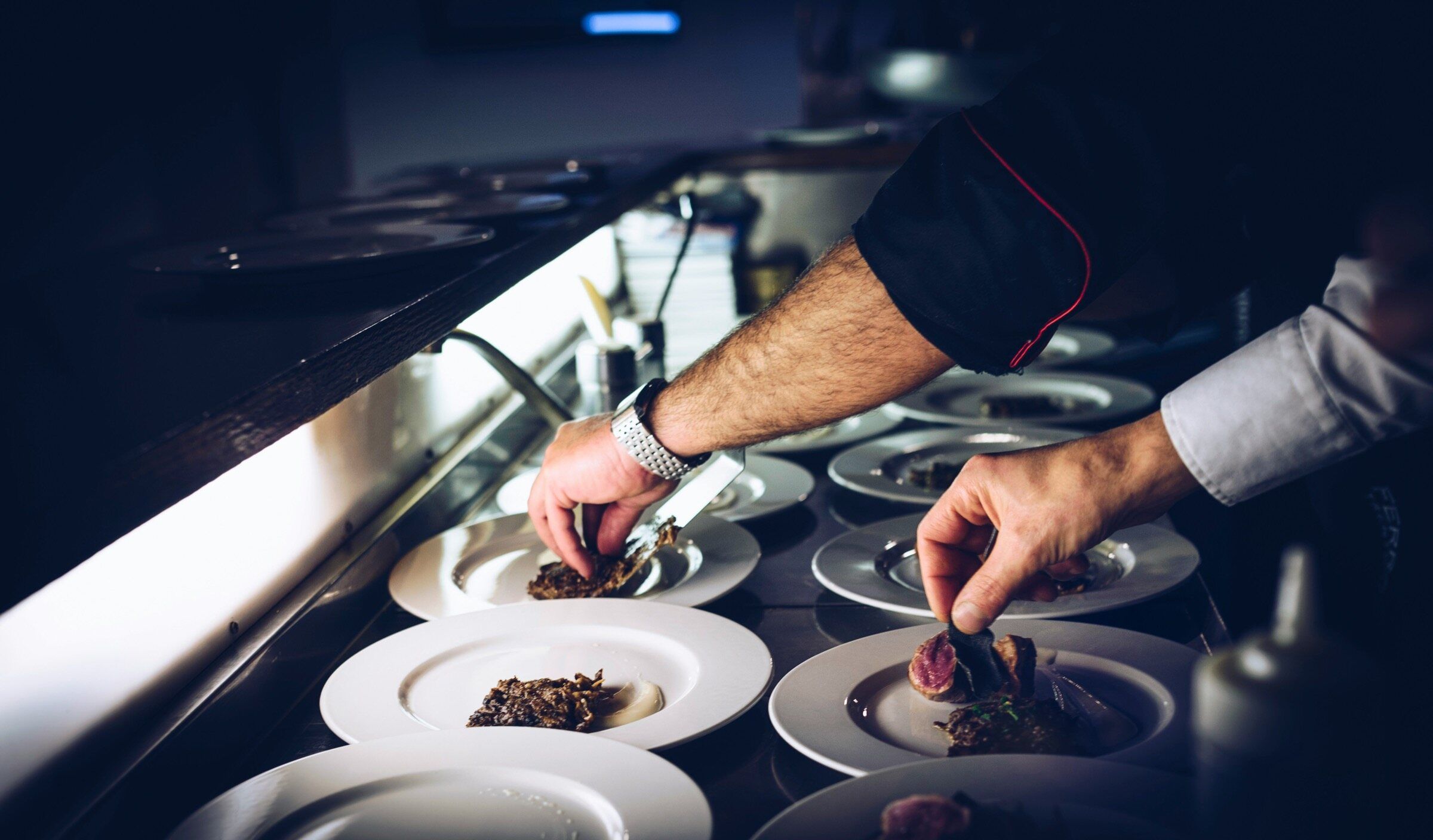 Hands plating dishes at the pass