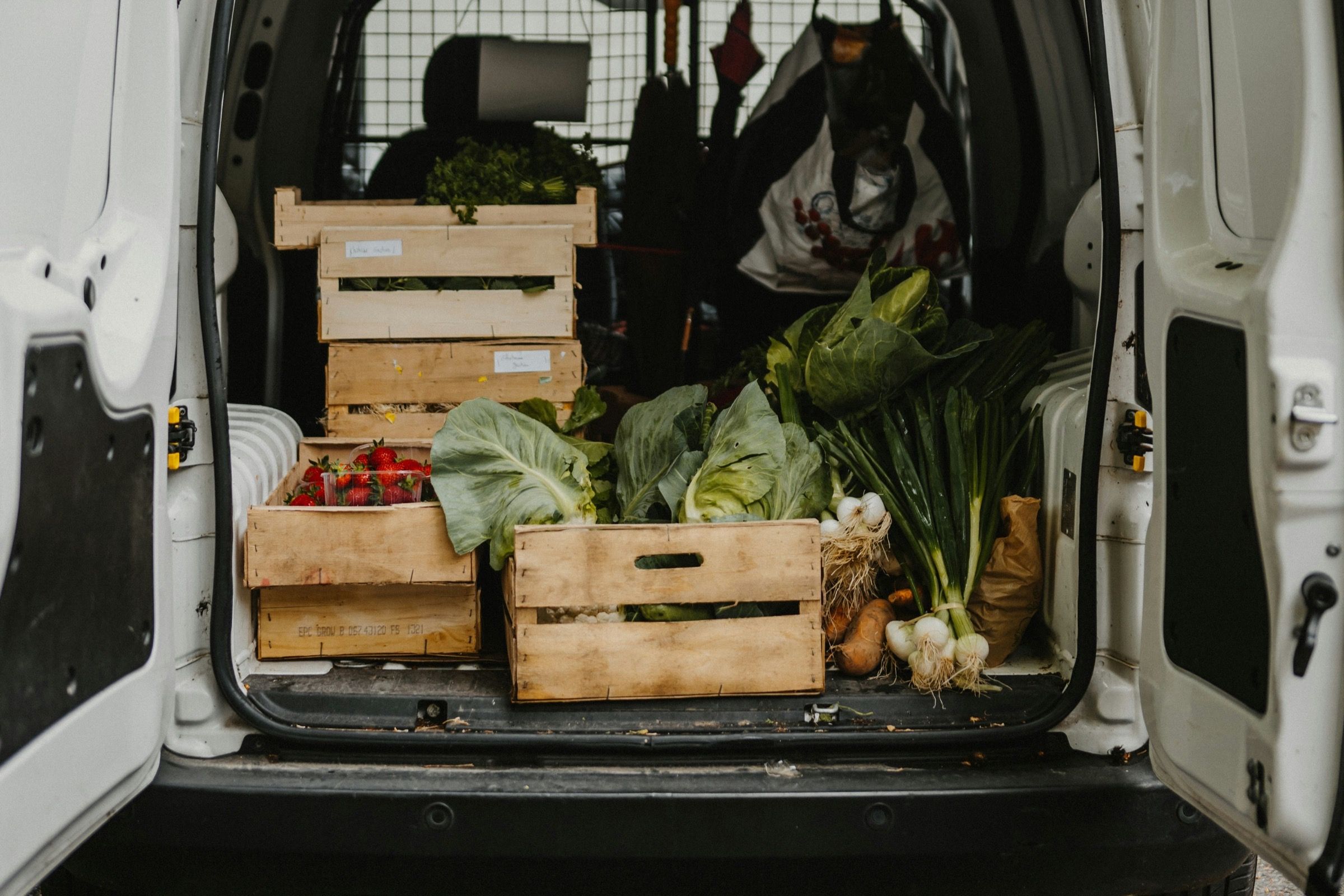 A delivery van with crates of fresh vegetables at a back door.